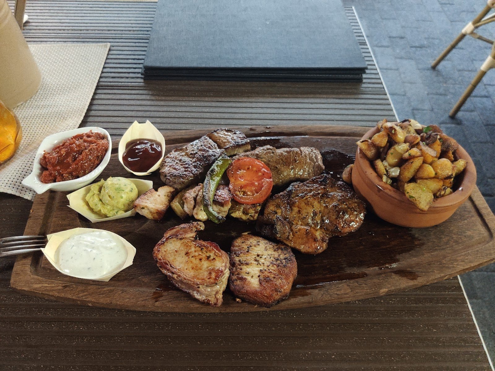Grillbrett mit mehreren Fleischsorten, gegrillter Tomate, Bratkartoffeln im Tontopf und Dips