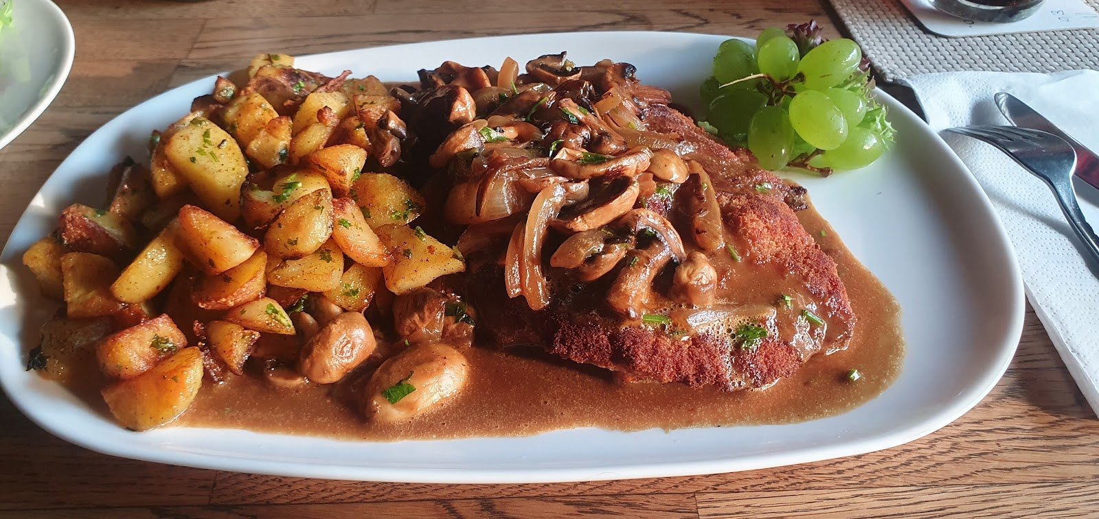 Schnitzel mit Pilzsoße und Bratkartoffeln, garniert mit Weintrauben