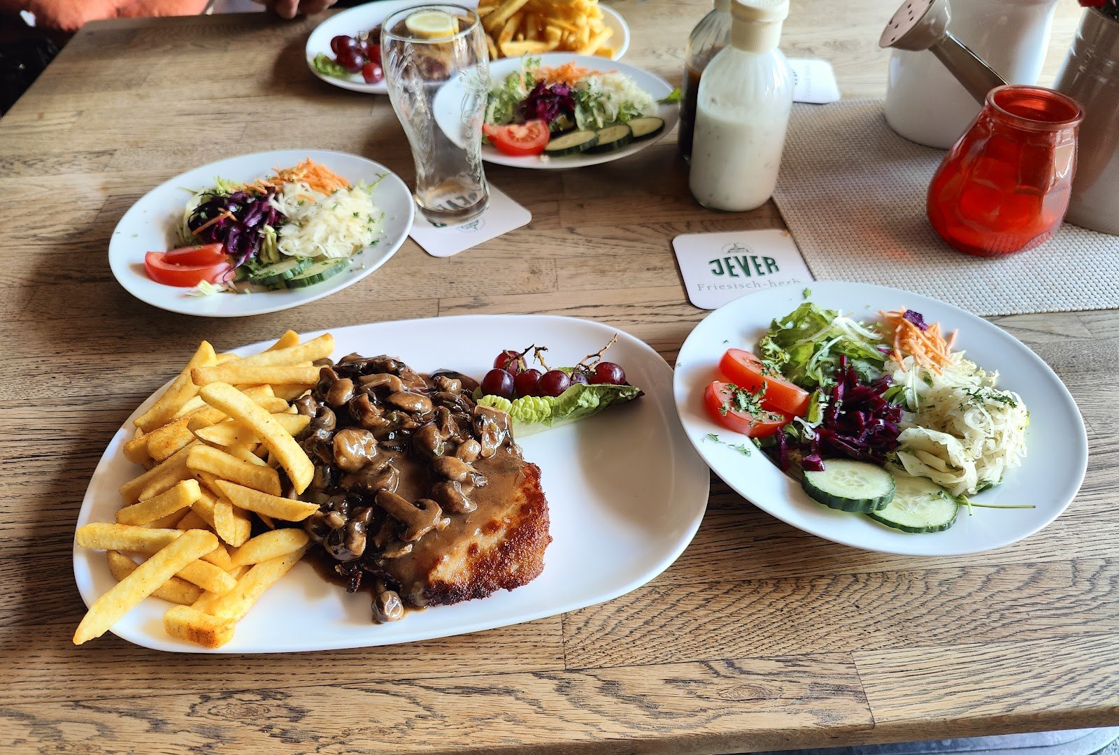 Schnitzel mit Pilzrahm und Pommes, daneben zwei Beilagensalate
