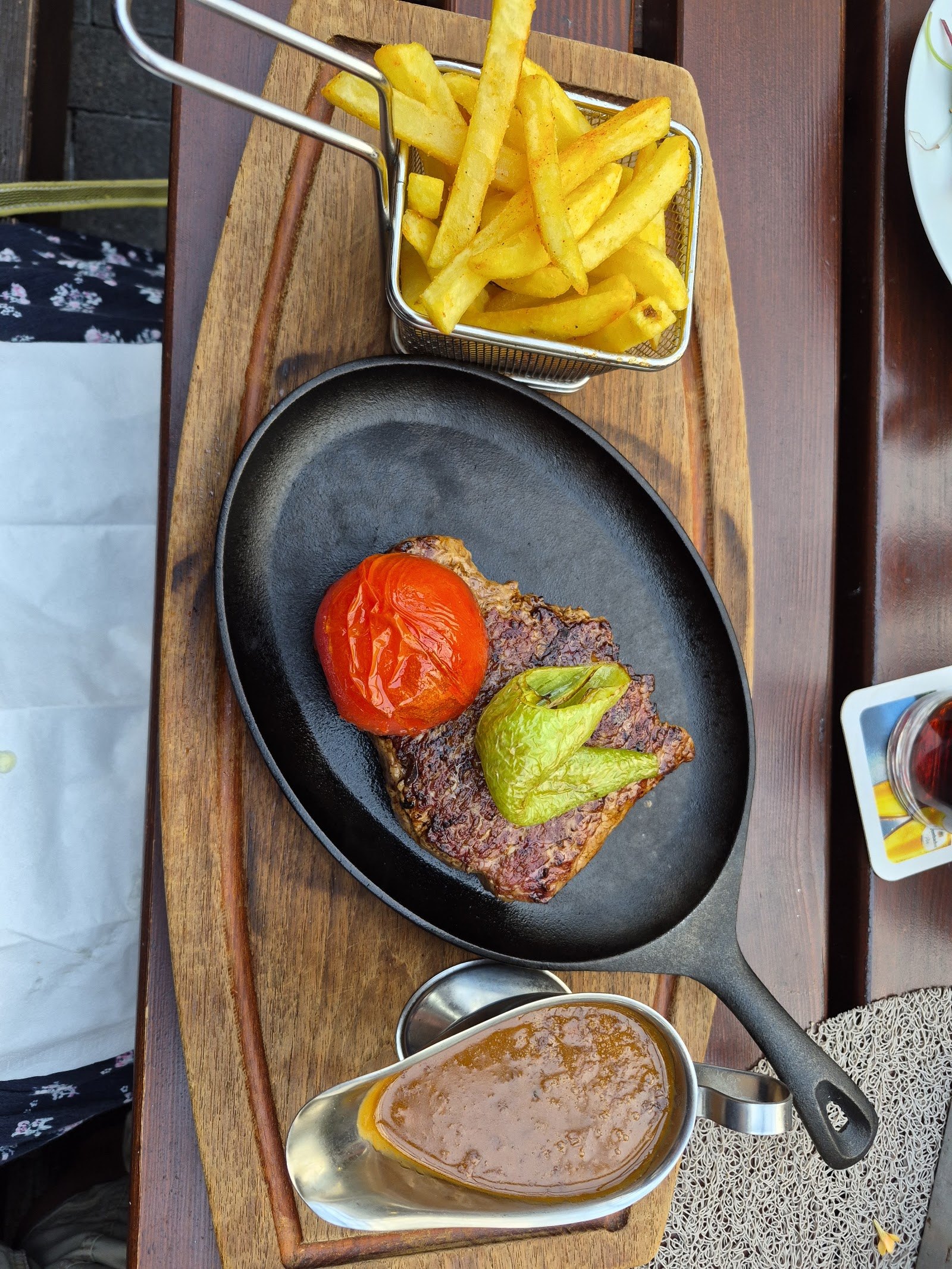 Steak in der gusseisernen Pfanne mit gegrillter Tomate und Kräuterbutter, Pommes im Körbchen und Soße im Kännchen